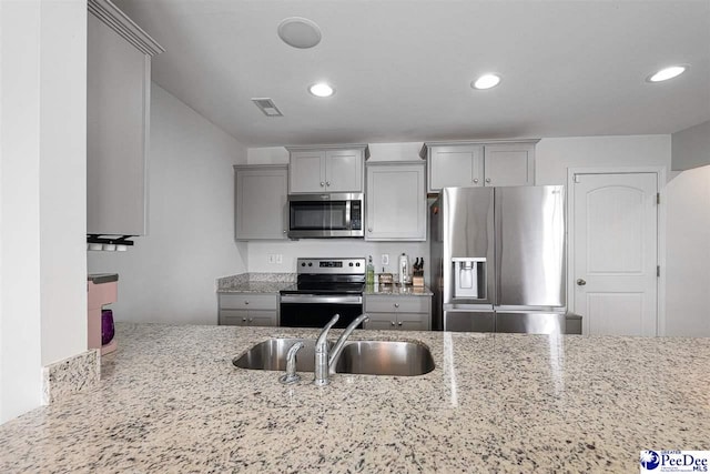 kitchen with visible vents, light stone counters, appliances with stainless steel finishes, gray cabinets, and a sink