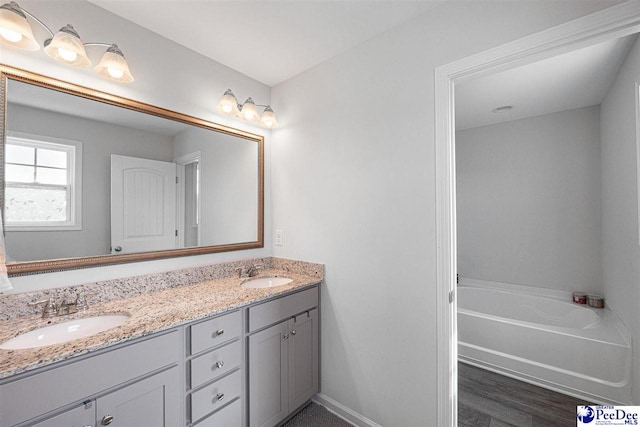 full bath featuring a bathtub, a sink, baseboards, and double vanity