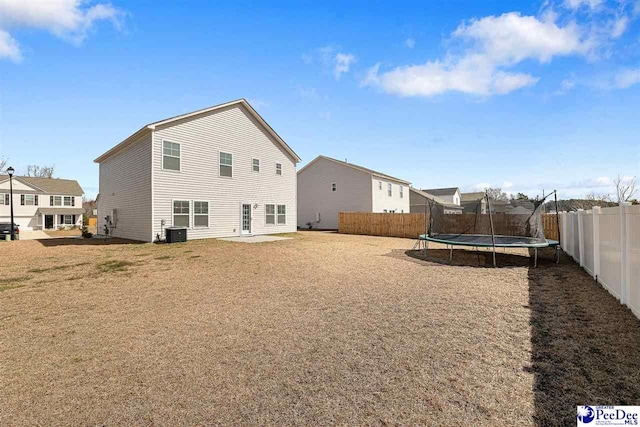 rear view of house featuring a trampoline, a yard, central AC, and fence