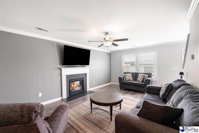 living room with baseboards, visible vents, a glass covered fireplace, wood finished floors, and crown molding