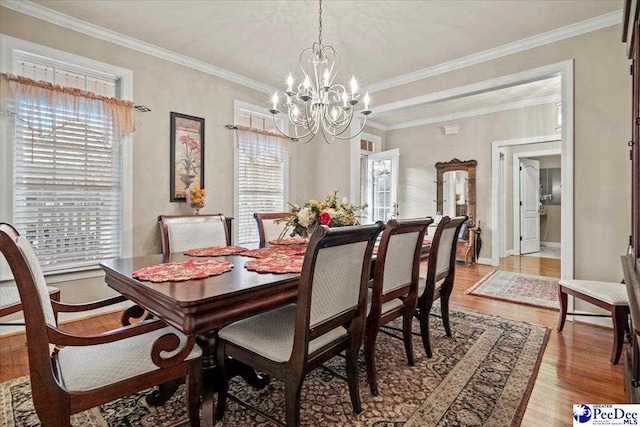 dining area featuring a notable chandelier, hardwood / wood-style flooring, a wealth of natural light, and ornamental molding