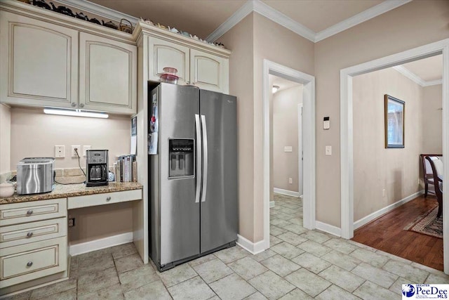 kitchen featuring cream cabinets, built in desk, ornamental molding, and stainless steel refrigerator with ice dispenser