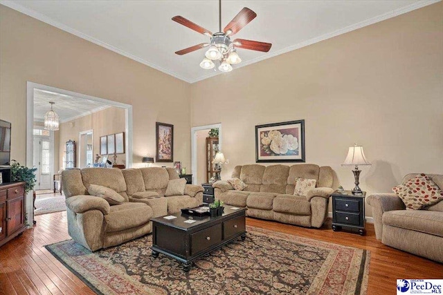 living room featuring crown molding, wood-type flooring, ceiling fan, and a towering ceiling