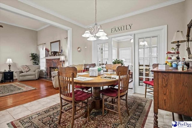 dining area with crown molding, a brick fireplace, light tile patterned floors, and a chandelier