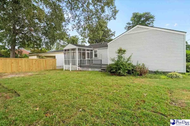 back of property with a wooden deck, a sunroom, and a lawn