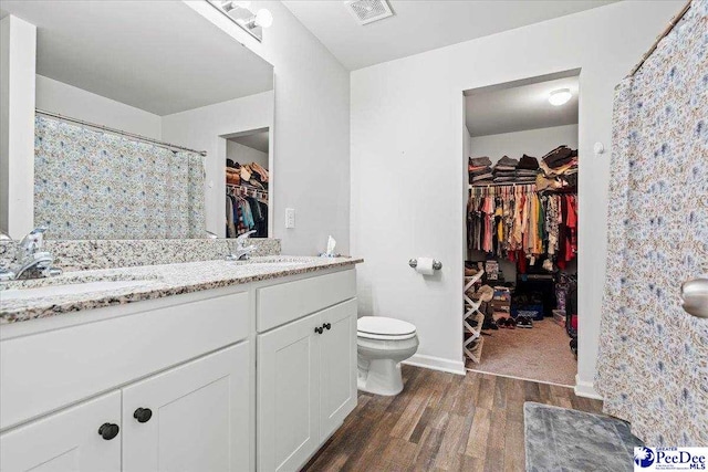 bathroom featuring toilet, wood finished floors, visible vents, a sink, and double vanity