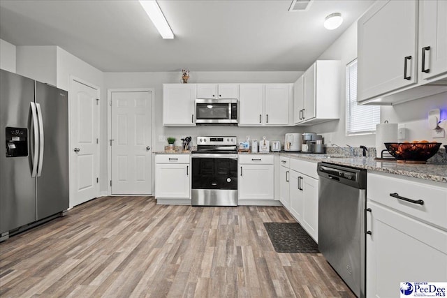 kitchen featuring appliances with stainless steel finishes, white cabinets, light wood-style floors, and visible vents