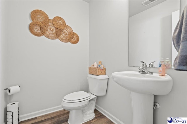 half bathroom featuring toilet, wood finished floors, visible vents, and baseboards