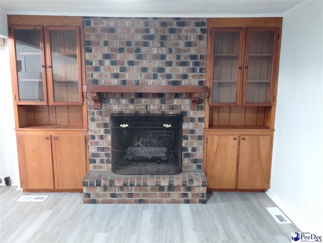 living room with crown molding, a brick fireplace, and light wood-type flooring