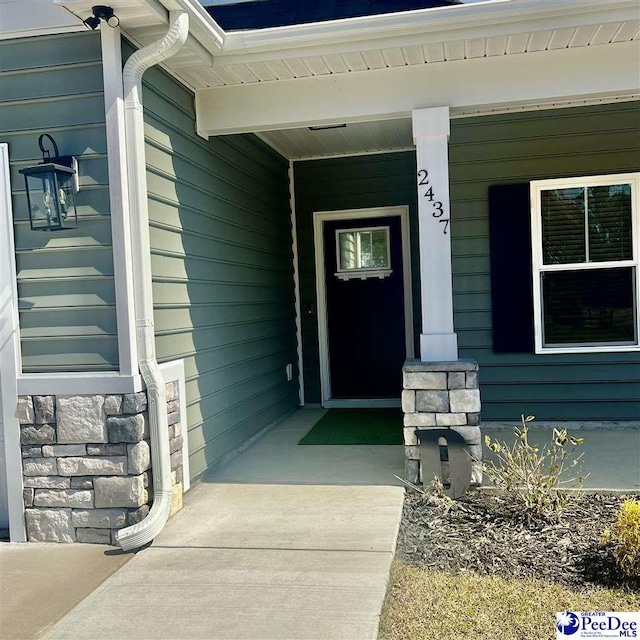 doorway to property with stone siding and covered porch