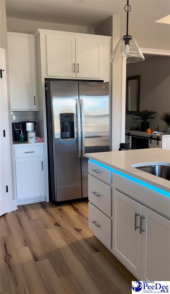 kitchen with light wood-style flooring, light countertops, stainless steel refrigerator with ice dispenser, white cabinetry, and decorative light fixtures