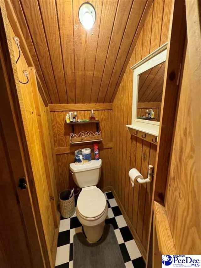 bathroom with wooden walls, toilet, wooden ceiling, tile patterned floors, and vaulted ceiling