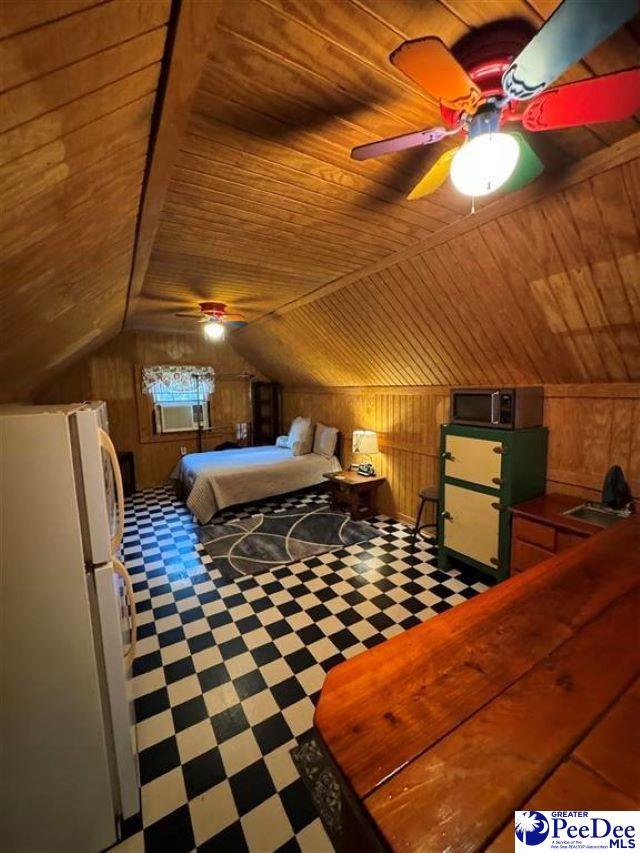 bedroom with wooden walls, lofted ceiling, wooden ceiling, tile patterned floors, and freestanding refrigerator