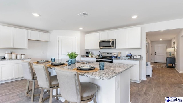 585 Strawberry Field Way, Galivants Ferry, SC 29544 - kitchen featuring appliances with stainless steel finishes, white cabinetry, a center island with sink, light wood-style flooring, and a breakfast bar area