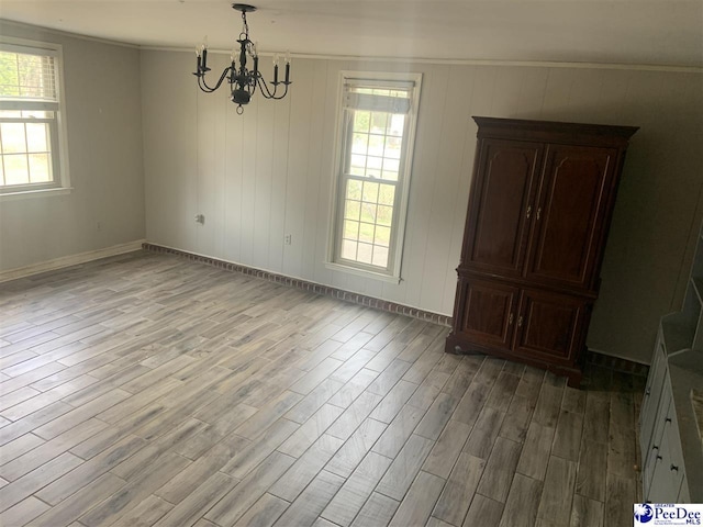 unfurnished dining area with an inviting chandelier, light wood-type flooring, a wealth of natural light, and crown molding