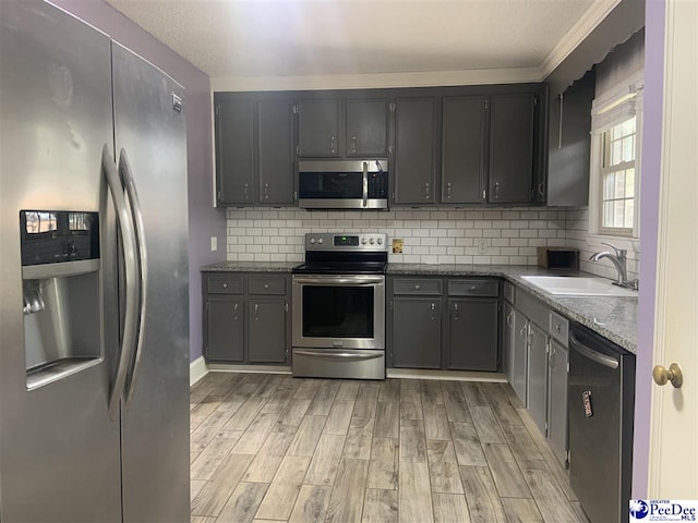 kitchen featuring appliances with stainless steel finishes, gray cabinetry, dark stone counters, decorative backsplash, and sink