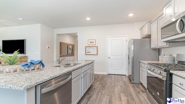 kitchen featuring light stone counters, a sink, a center island with sink, stainless steel appliances, and light wood-type flooring