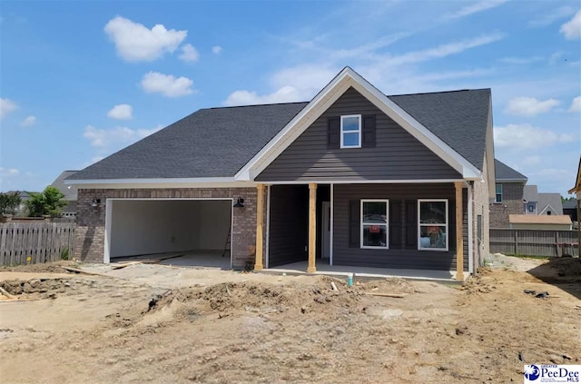 view of front of home featuring an attached garage, fence, roof with shingles, brick siding, and a porch