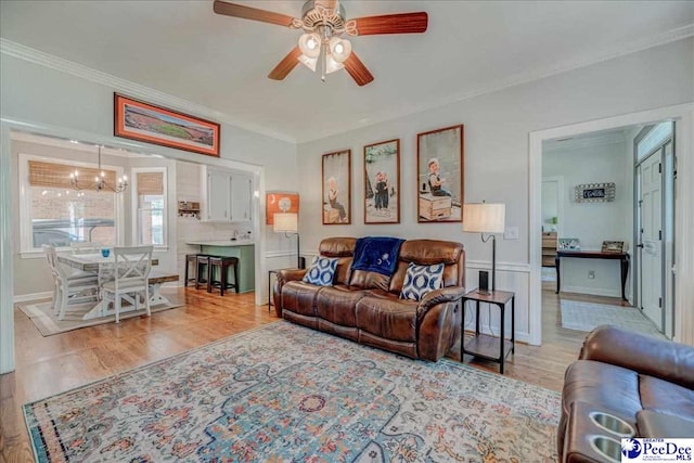 living room featuring light wood-style flooring, ceiling fan with notable chandelier, and ornamental molding