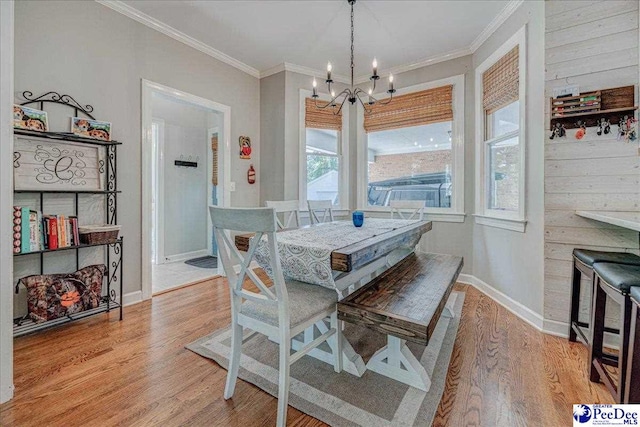 dining space with light wood-style flooring, a notable chandelier, ornamental molding, and baseboards