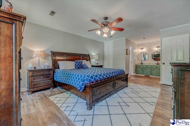 bedroom with light wood-type flooring, crown molding, baseboards, and ensuite bath