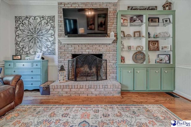 living area with visible vents, ornamental molding, a fireplace, wainscoting, and wood finished floors