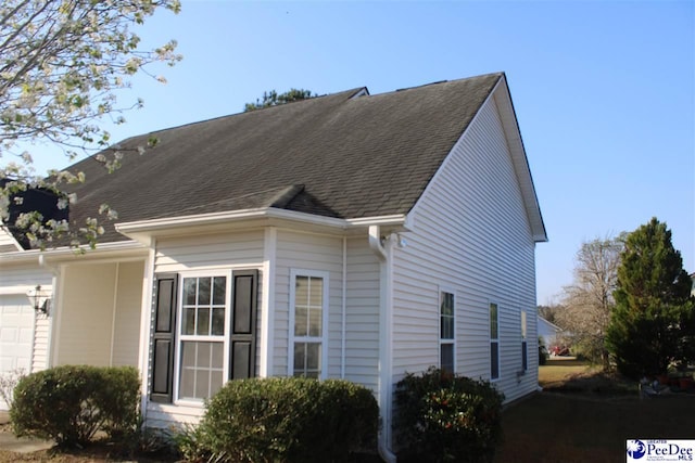 view of side of home with a shingled roof and a garage