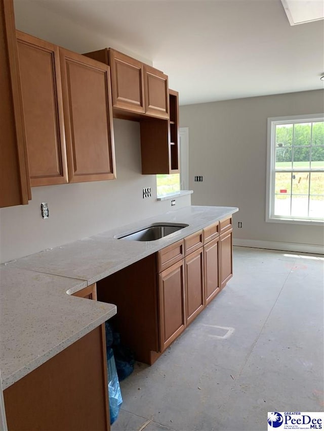 kitchen featuring concrete floors, brown cabinets, and light stone counters