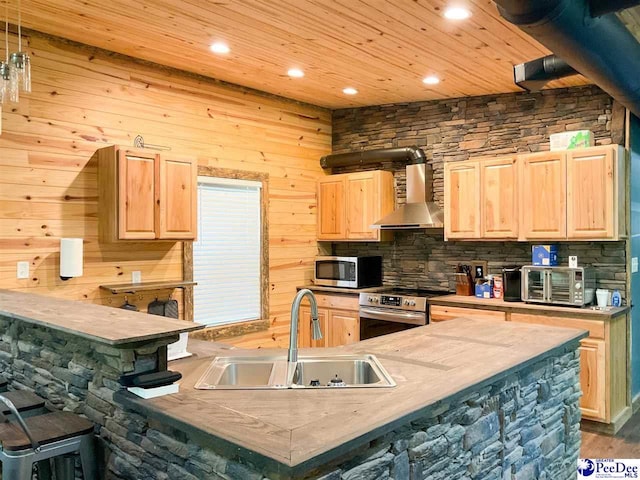 kitchen with recessed lighting, light brown cabinetry, stainless steel appliances, a sink, and wall chimney exhaust hood