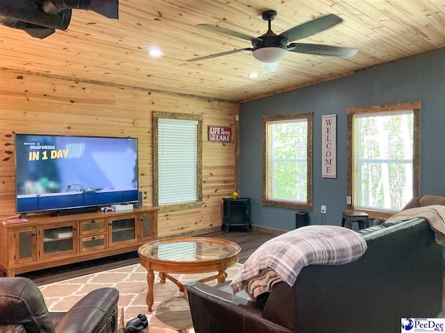 living area with wood walls, a ceiling fan, a wood stove, and wooden ceiling