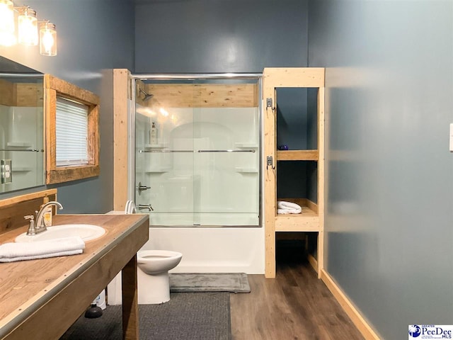 full bath with combined bath / shower with glass door, wood finished floors, toilet, and a sink