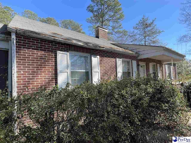 view of side of property featuring a chimney and brick siding