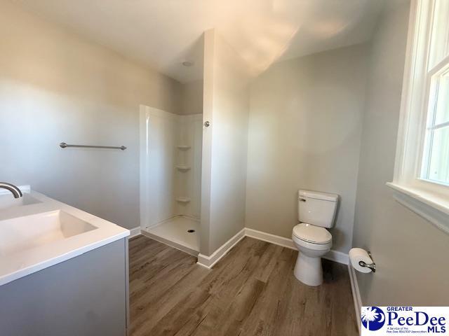 bathroom with baseboards, toilet, wood finished floors, walk in shower, and a sink