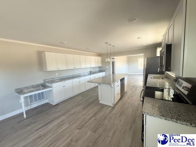 kitchen featuring white cabinets, appliances with stainless steel finishes, a center island, crown molding, and light wood-style floors