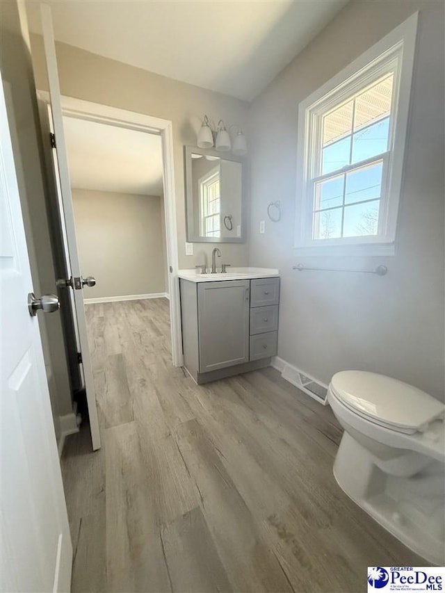 half bath with visible vents, toilet, vanity, wood finished floors, and baseboards