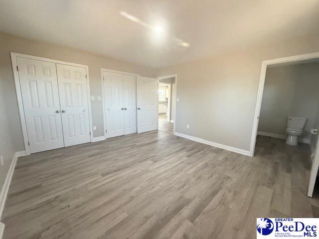 unfurnished bedroom featuring wood finished floors, two closets, and baseboards