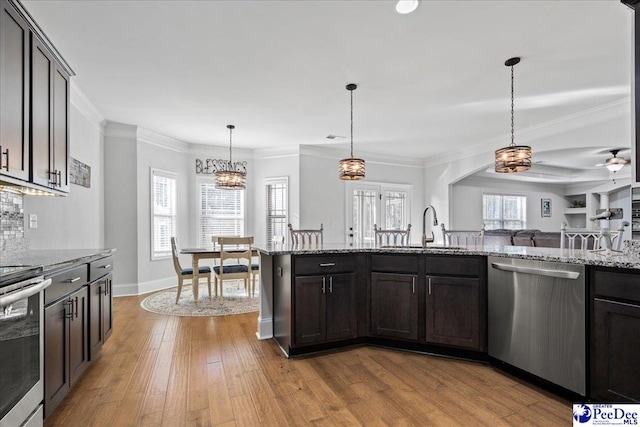 kitchen featuring appliances with stainless steel finishes, sink, hanging light fixtures, light stone counters, and dark brown cabinets