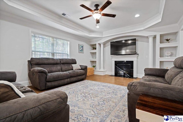 living room with ornate columns, ornamental molding, a tray ceiling, built in features, and hardwood / wood-style flooring