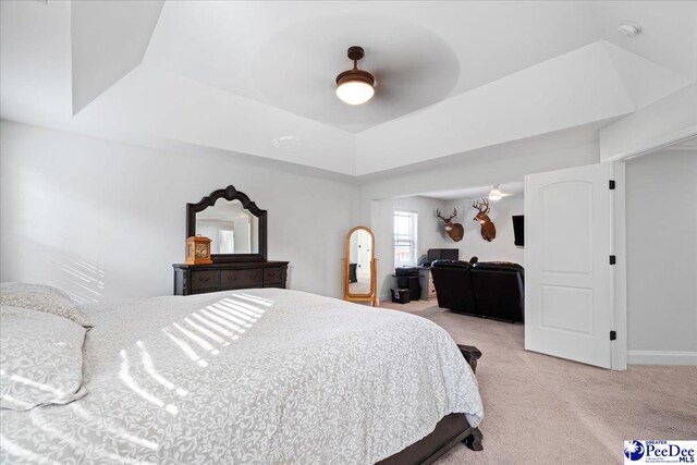 bedroom featuring light carpet, ceiling fan, and a tray ceiling