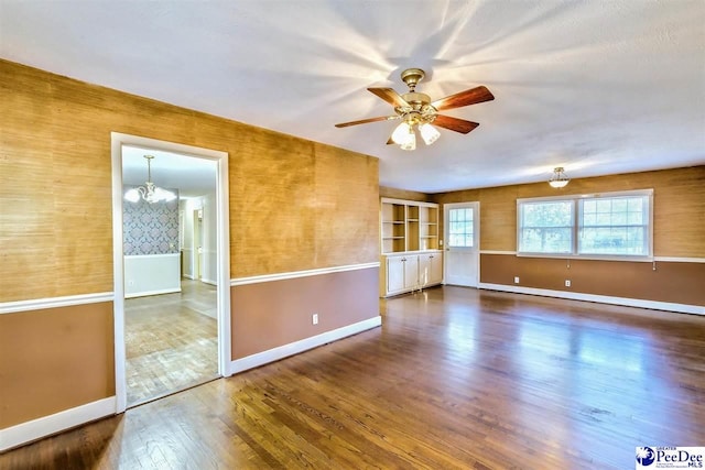 spare room with dark wood-type flooring and ceiling fan with notable chandelier