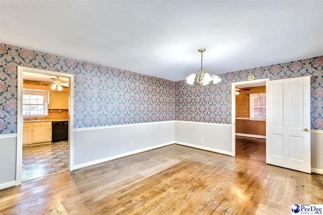 empty room featuring sink, a notable chandelier, a textured ceiling, and light wood-type flooring