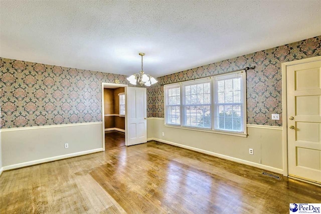 unfurnished dining area featuring hardwood / wood-style flooring, an inviting chandelier, and a textured ceiling