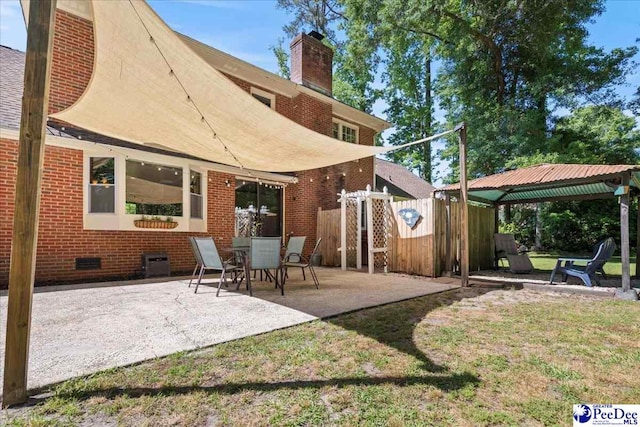 rear view of house featuring a chimney, fence, a gazebo, brick siding, and a patio area