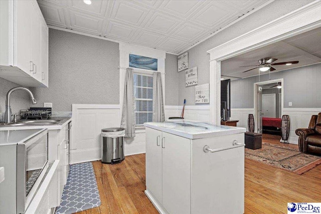 kitchen with sink, light wood-type flooring, a kitchen island, ceiling fan, and white cabinets