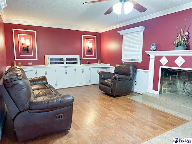 living room featuring crown molding, light hardwood / wood-style flooring, a textured ceiling, a tile fireplace, and ceiling fan