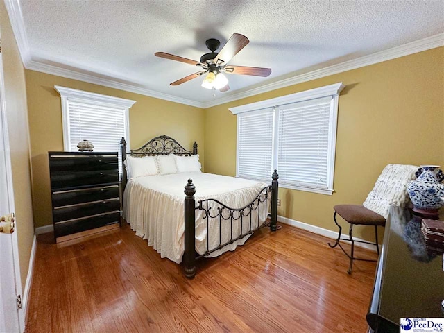 bedroom featuring multiple windows, ornamental molding, wood-type flooring, and a textured ceiling