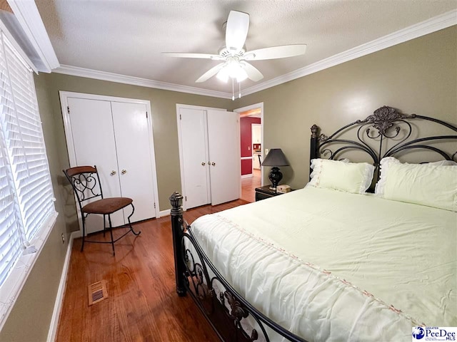 bedroom featuring a textured ceiling, multiple closets, ornamental molding, ceiling fan, and hardwood / wood-style floors