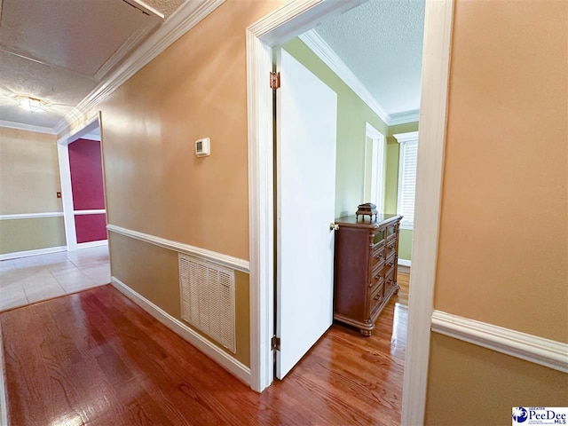 hallway featuring ornamental molding, a textured ceiling, and light wood-type flooring