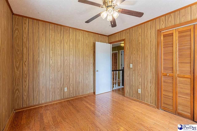 unfurnished bedroom with a closet, ornamental molding, wooden walls, and light hardwood / wood-style flooring