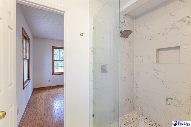 bathroom with a tile shower, hardwood / wood-style floors, and a textured ceiling